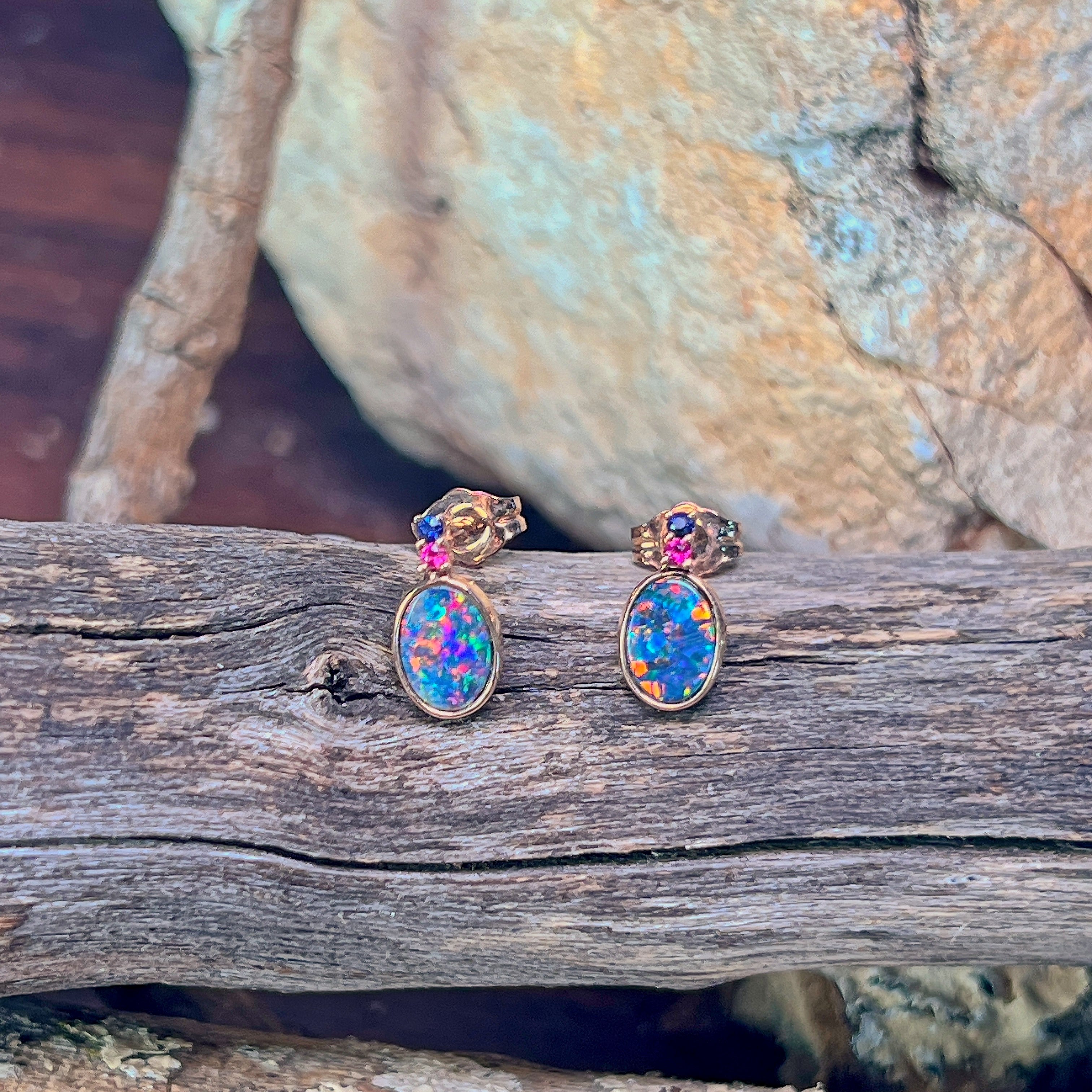 Pair of 14kt rose gold opal doublet stud earrings resting on driftwood and sandstone