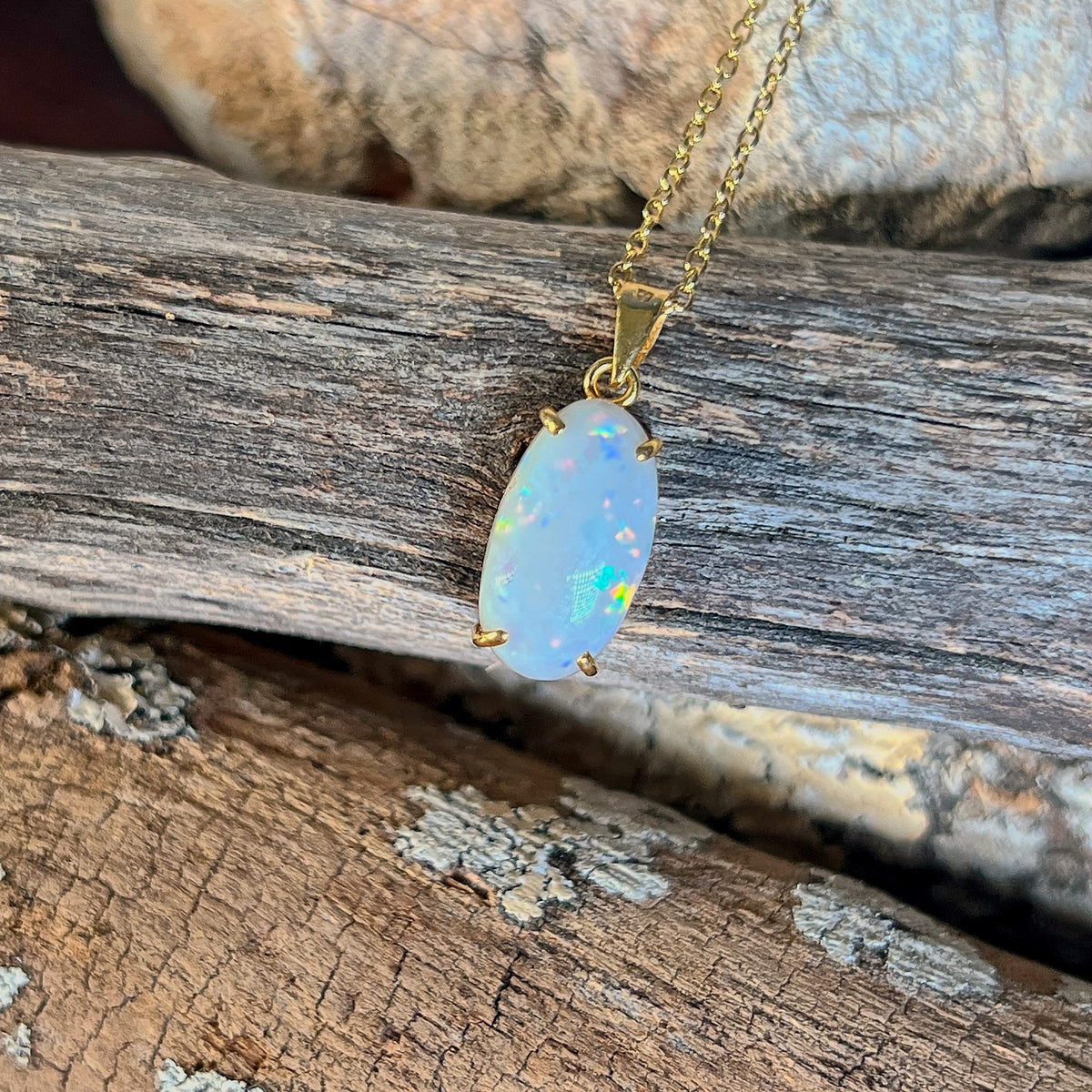 Claw set Australian white opal pendant in 18kt yellow gold on weathered timber