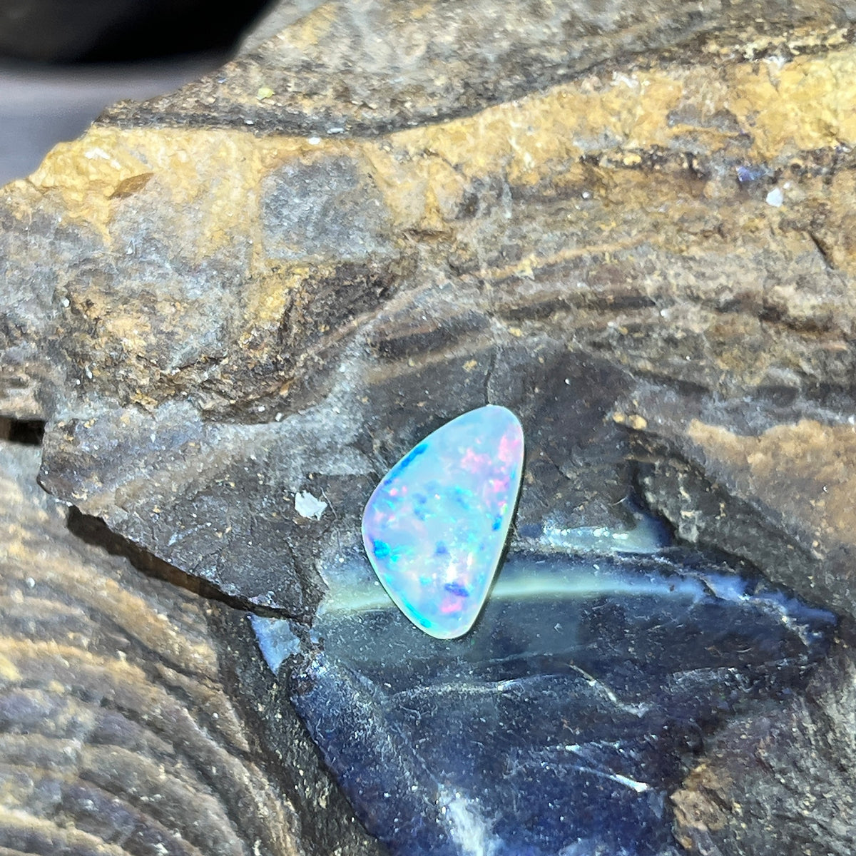 1.36ct triangular crystal opal loose stone, green, red and blue flashes, unset, on rock