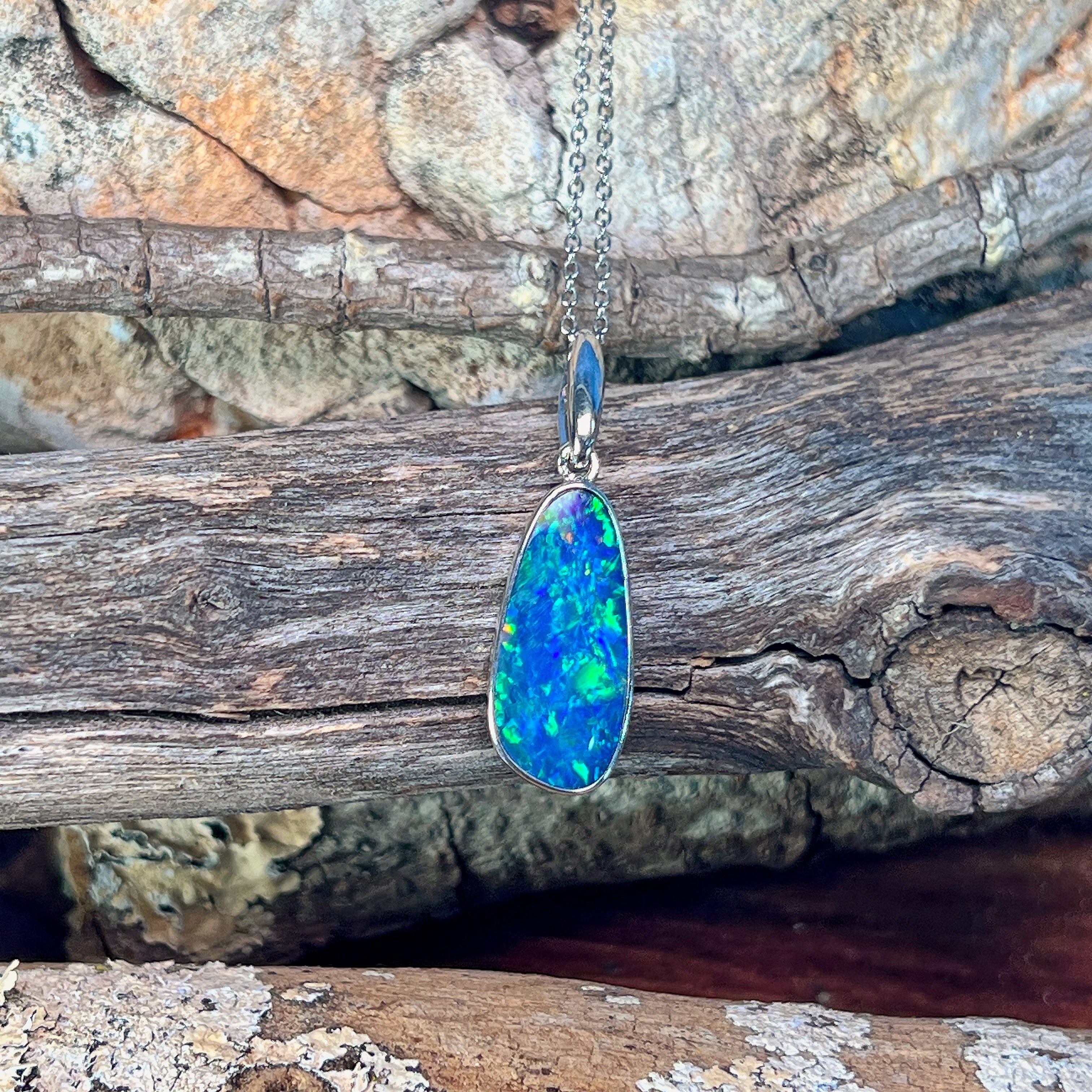 Sterling silver freeform opal doublet pendant hanging against weathered driftwood