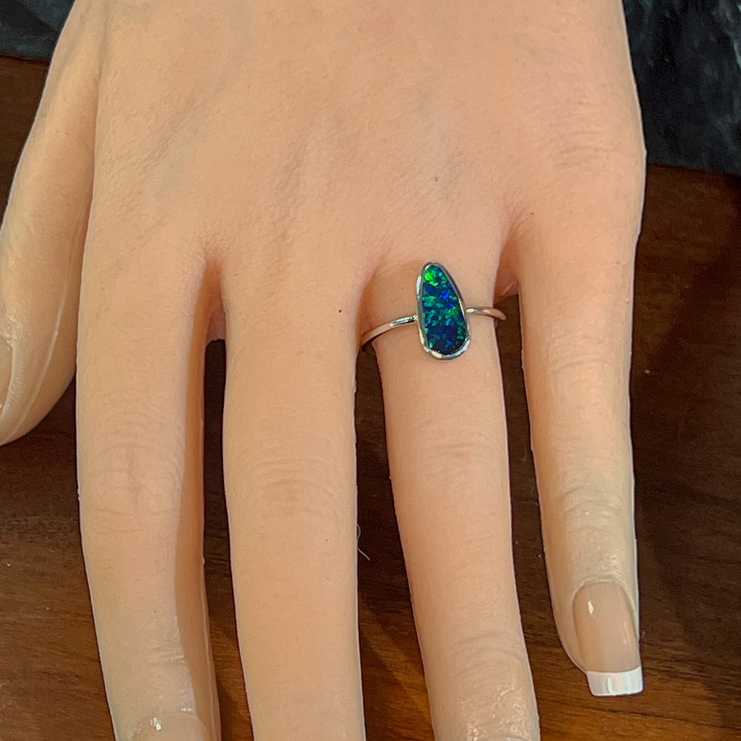 Blue-green freeform opal doublet ring worn on the hand, viewed across the fingers
