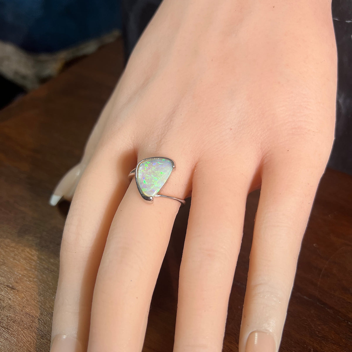 Triangular solid crystal opal ring in sterling silver, size O, green and blue play-of-colour, worn on a display hand