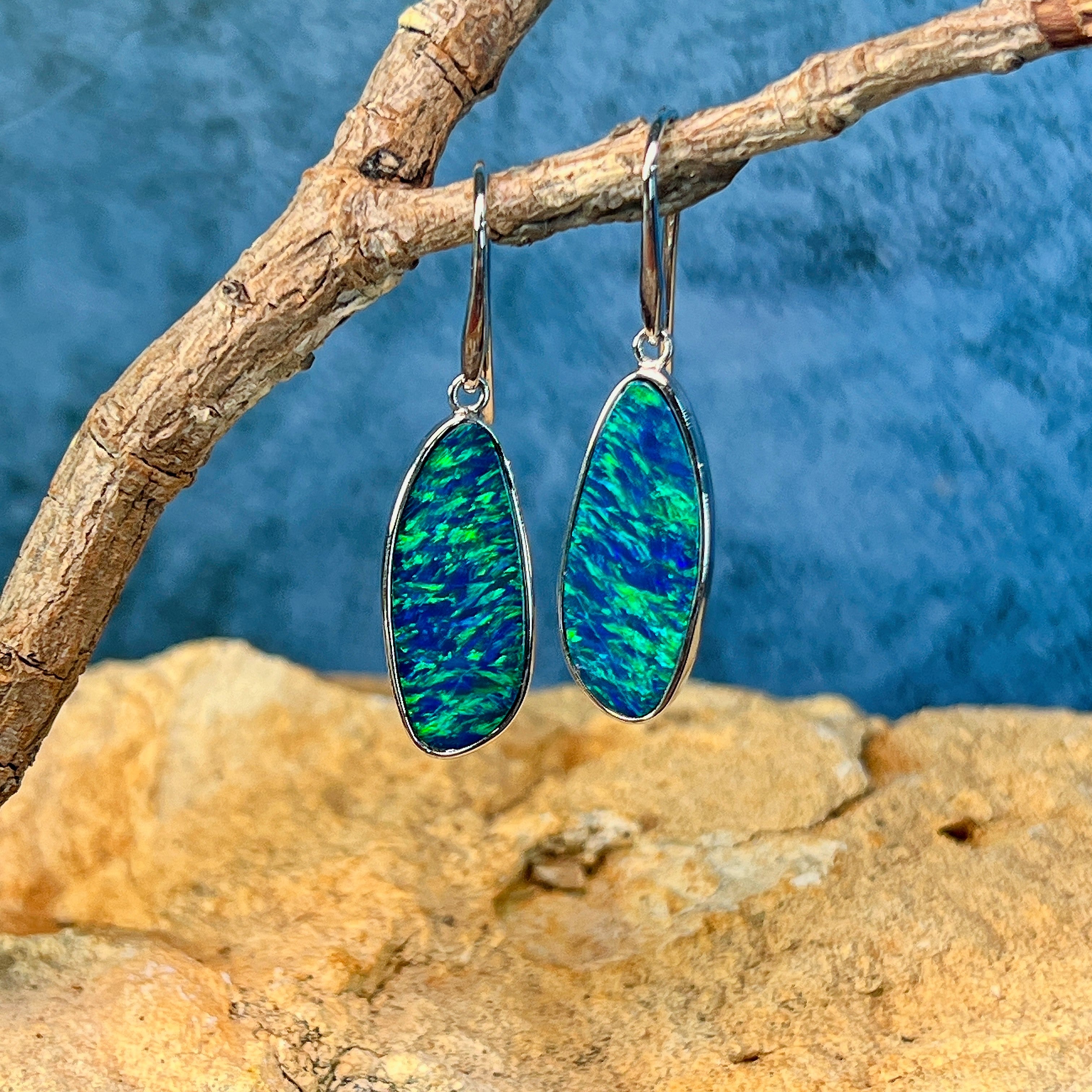 White gold opal doublet drop earrings in close view, green and blue flash across the stones