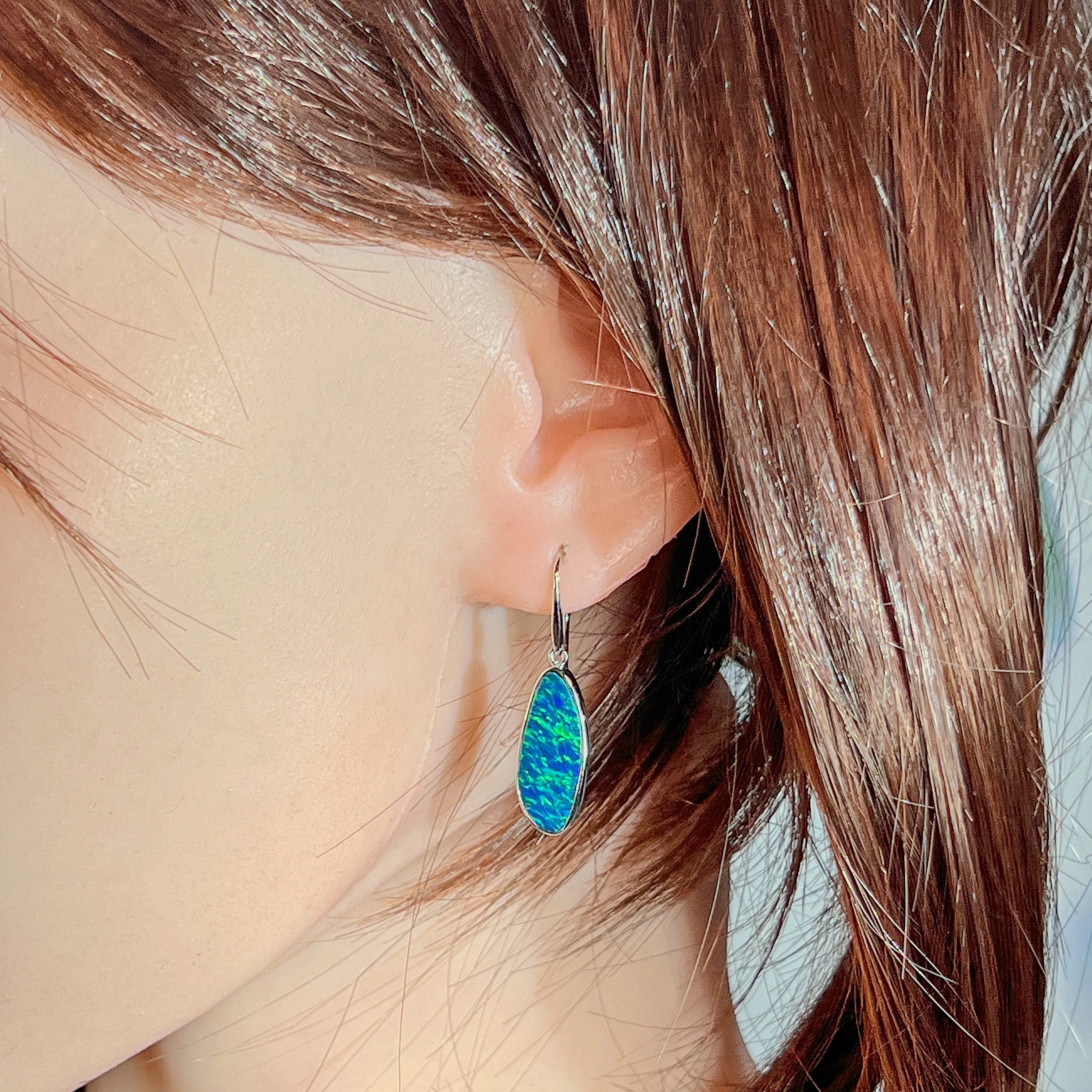 Green-blue opal doublet drop earring worn on the ear beneath loose hair