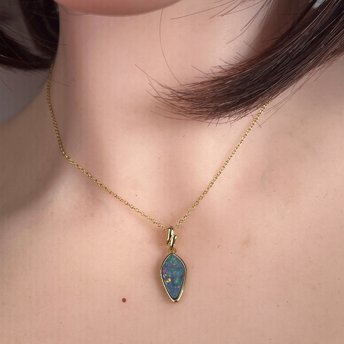 16 x 8mm oval Australian opal doublet pendant worn at the neck, yellow gold-plated silver