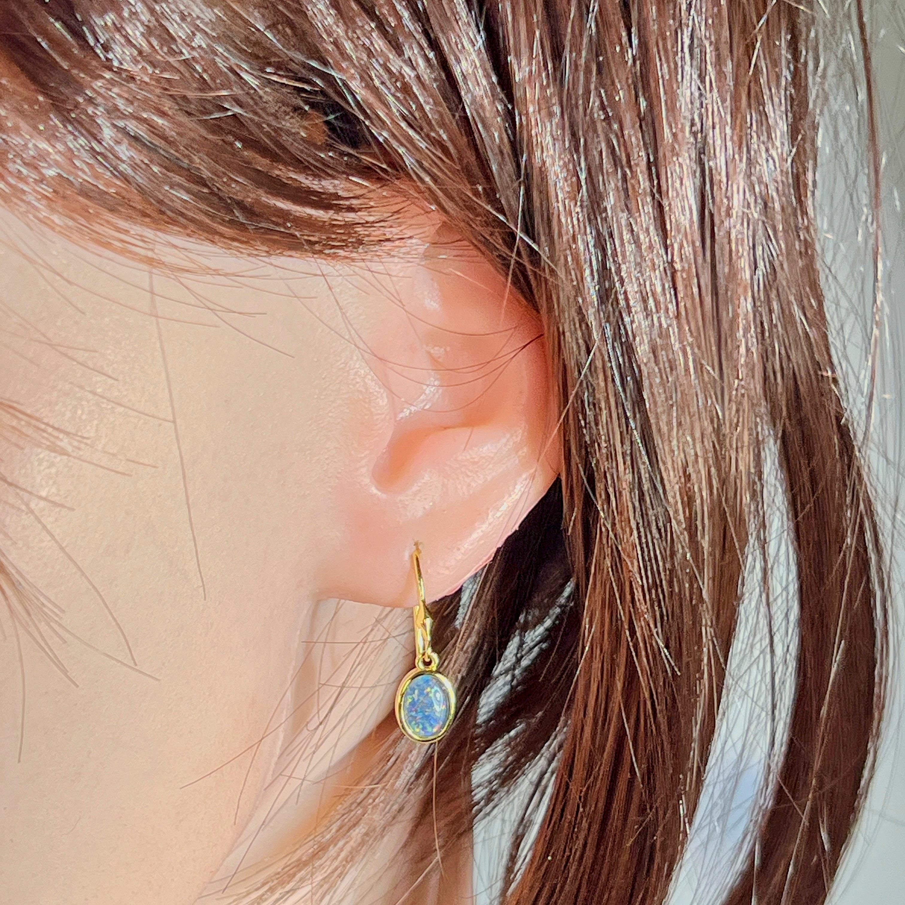 Ear close-up of the yellow gold plated dangling earring with oval Australian opal triplet