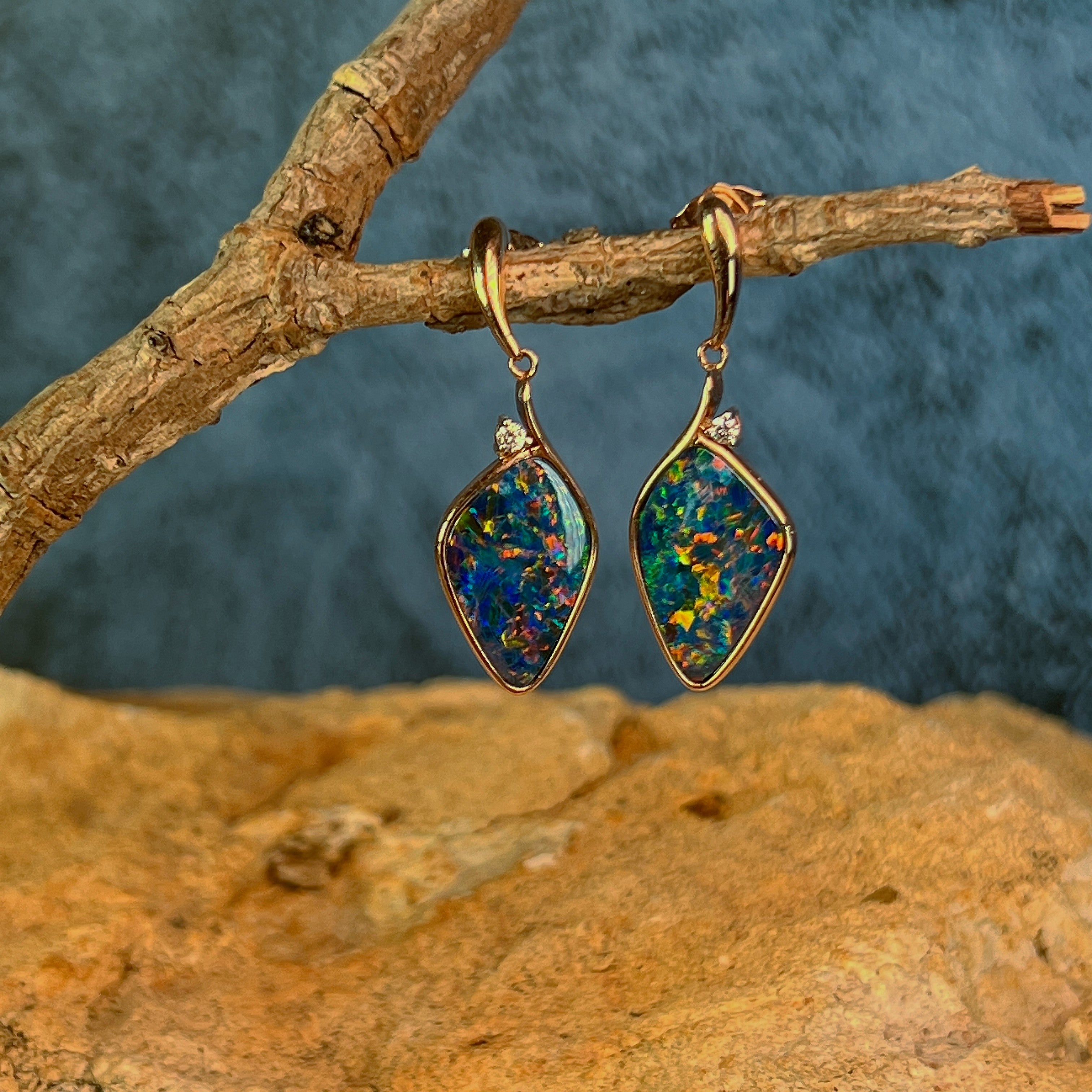 Pair of rose gold opal doublet drop earrings viewed level against a dark background