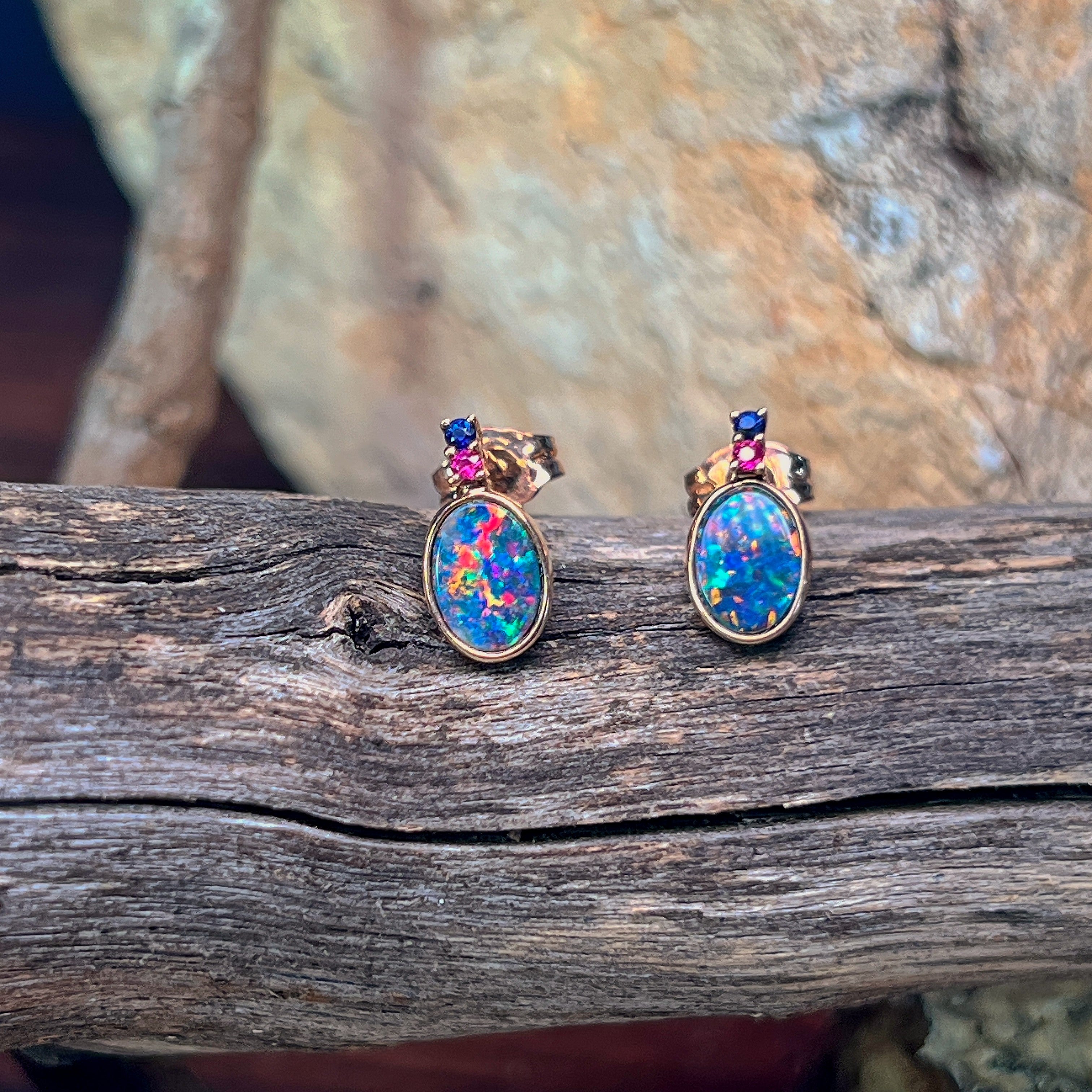 Rose gold oval opal doublet studs with ruby and sapphire accents on weathered driftwood