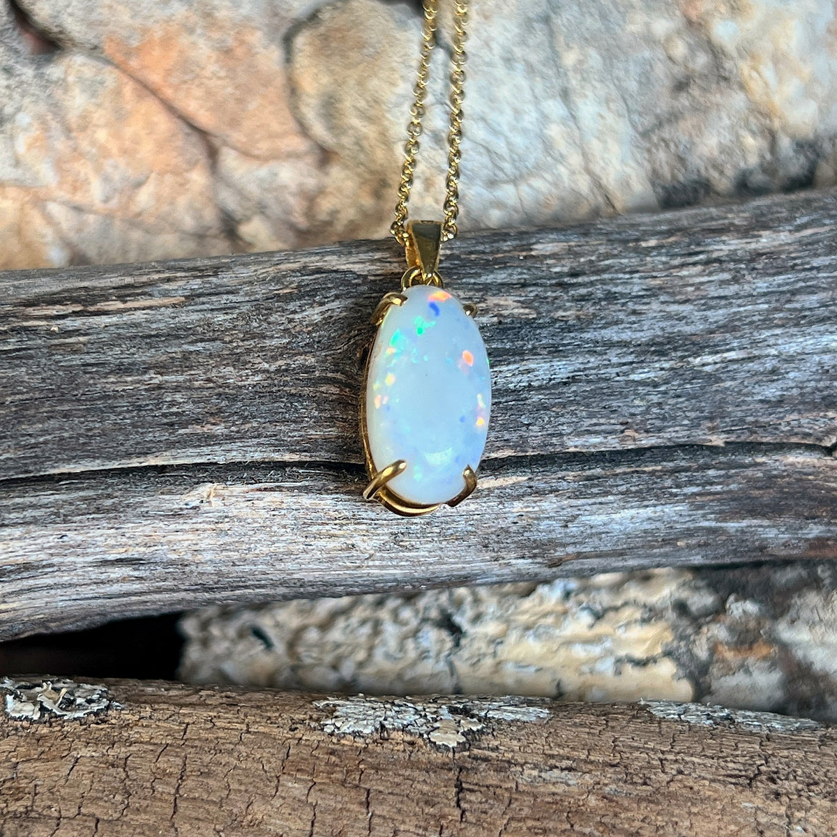 Close view of an oval Australian white opal in an 18kt yellow gold pendant, red and blue pinfire