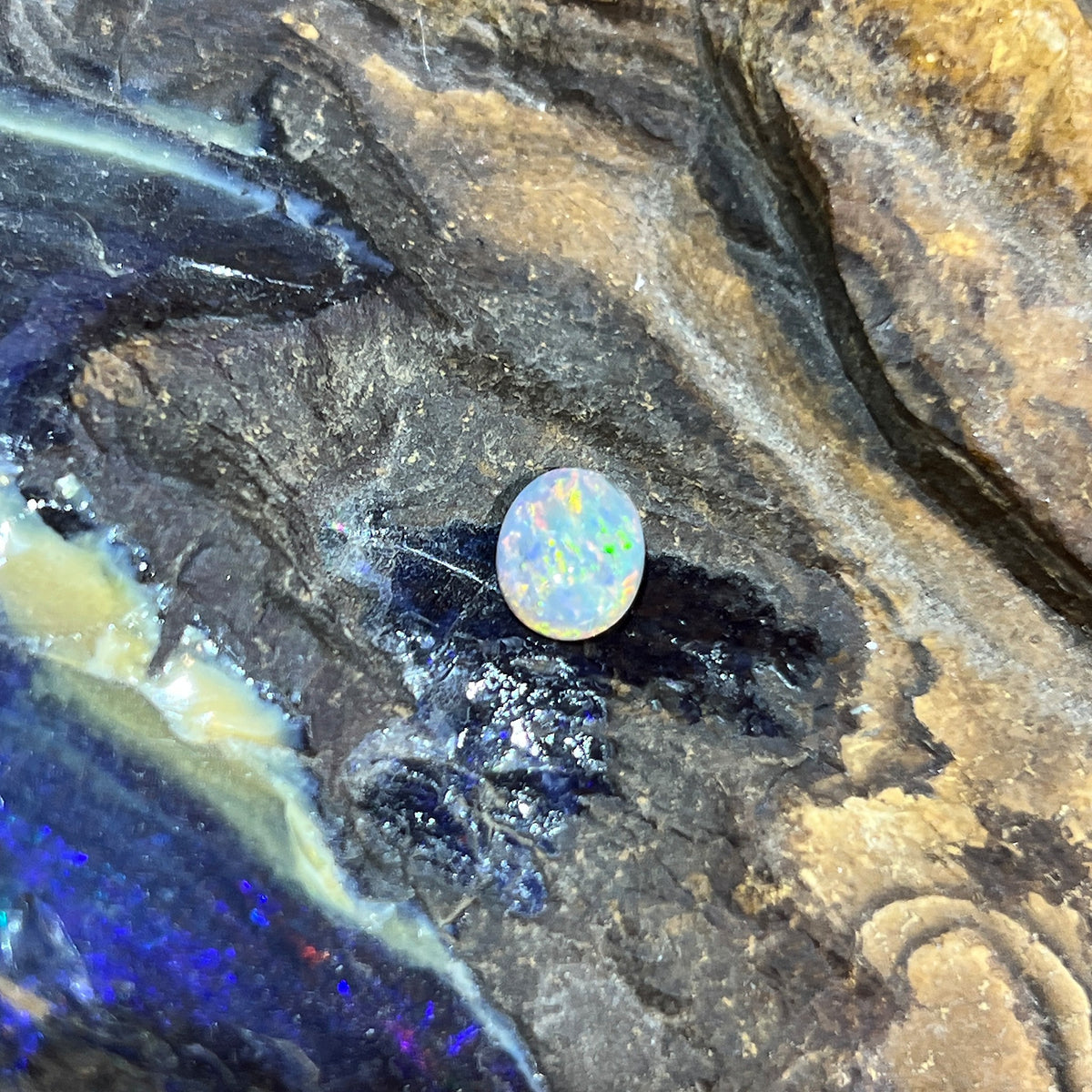 Solid Australian black opal 0.85ct, oval 8.2x6.8mm, red, orange and yellow flashes on a grey base, loose stone on rock