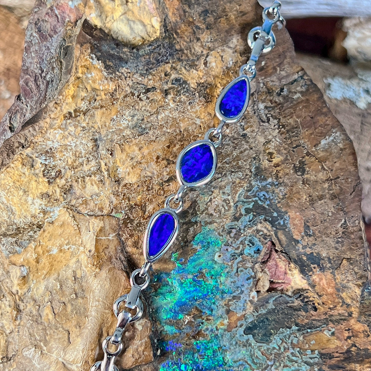 Sterling silver bracelet with three opal doublets photographed in profile against rock, showing the bezel settings