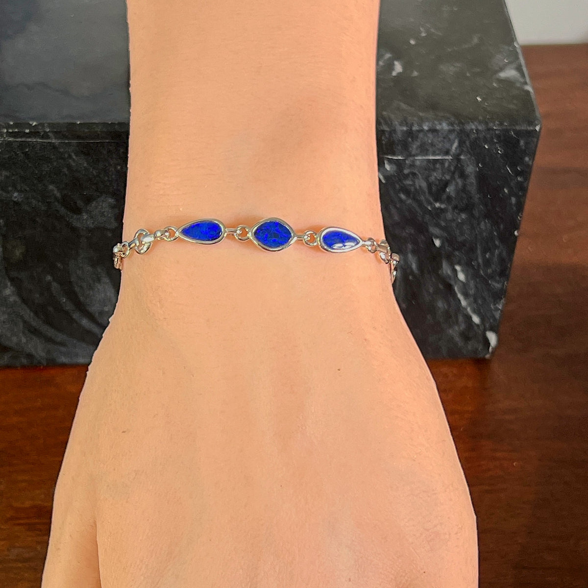 Sterling silver bracelet with three opal doublets worn on the wrist, full view of the linked stones