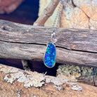 Blue-green opal doublet pendant necklace in sterling silver resting on weathered driftwood