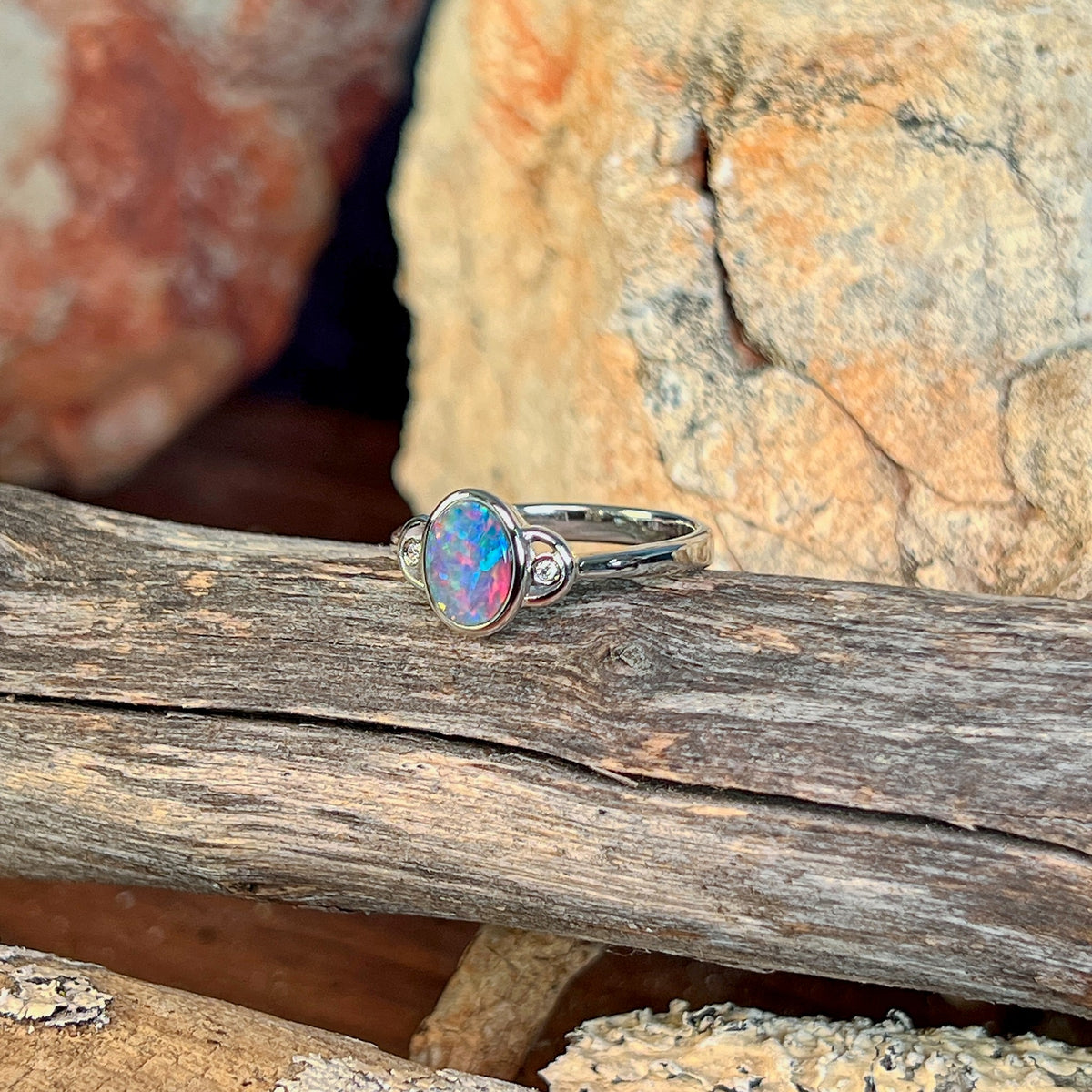 Oval opal doublet ring in silver photographed in profile on driftwood, showing the setting