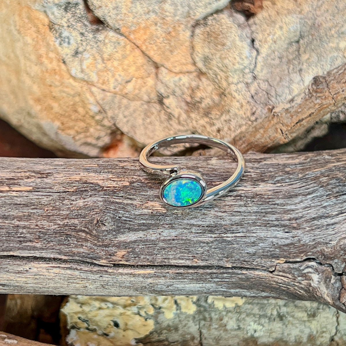 Slanted oval opal doublet ring in silver photographed in profile on driftwood, showing the setting