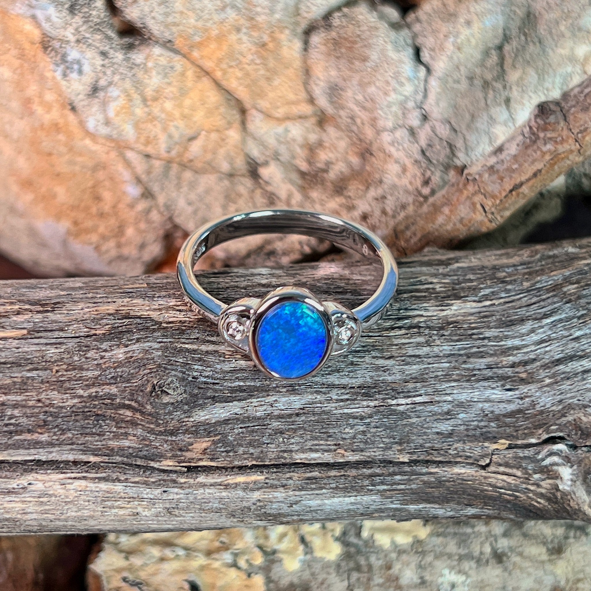 Blue opal doublet ring in silver photographed in profile on driftwood, showing the setting