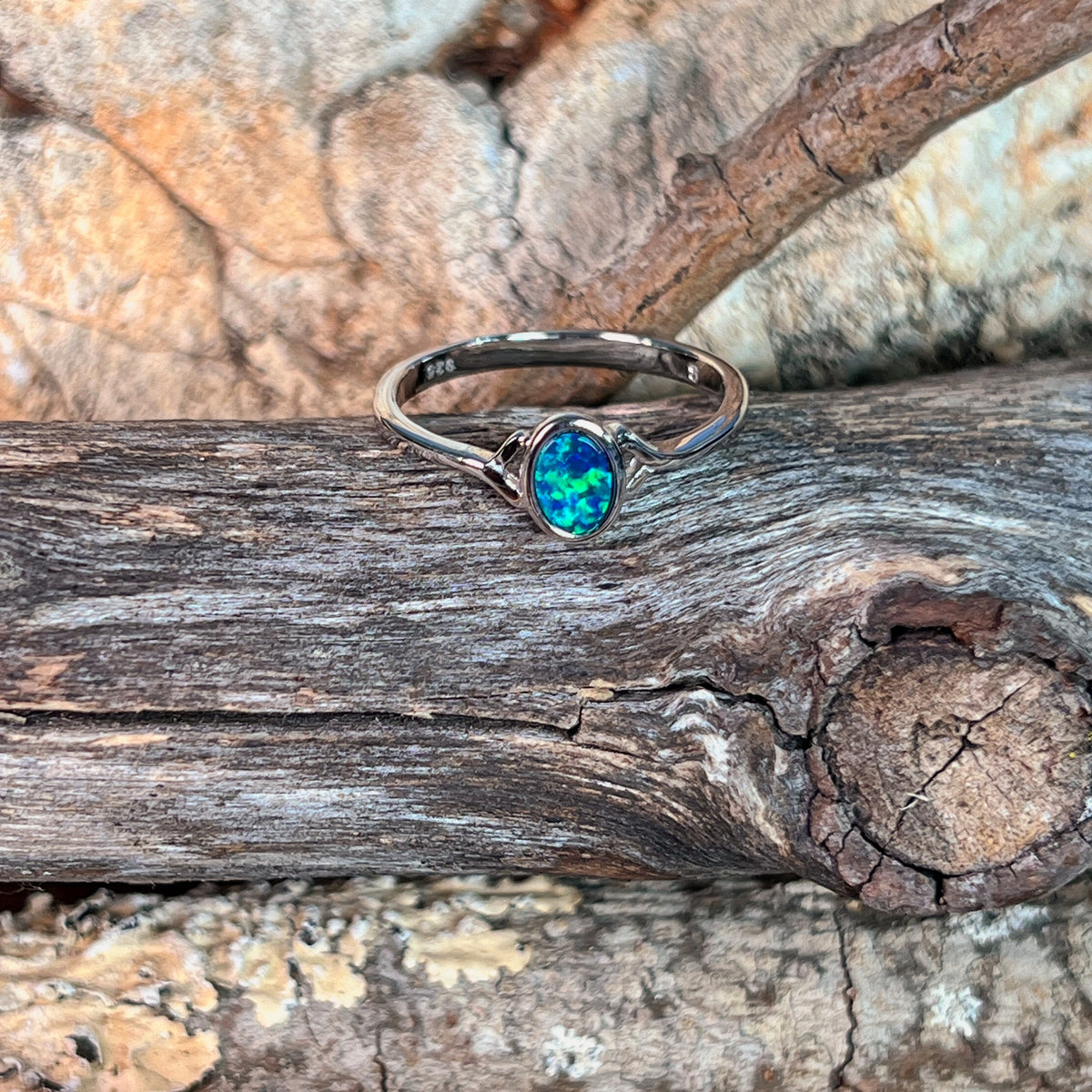 Deep green opal doublet ring in silver resting on weathered driftwood