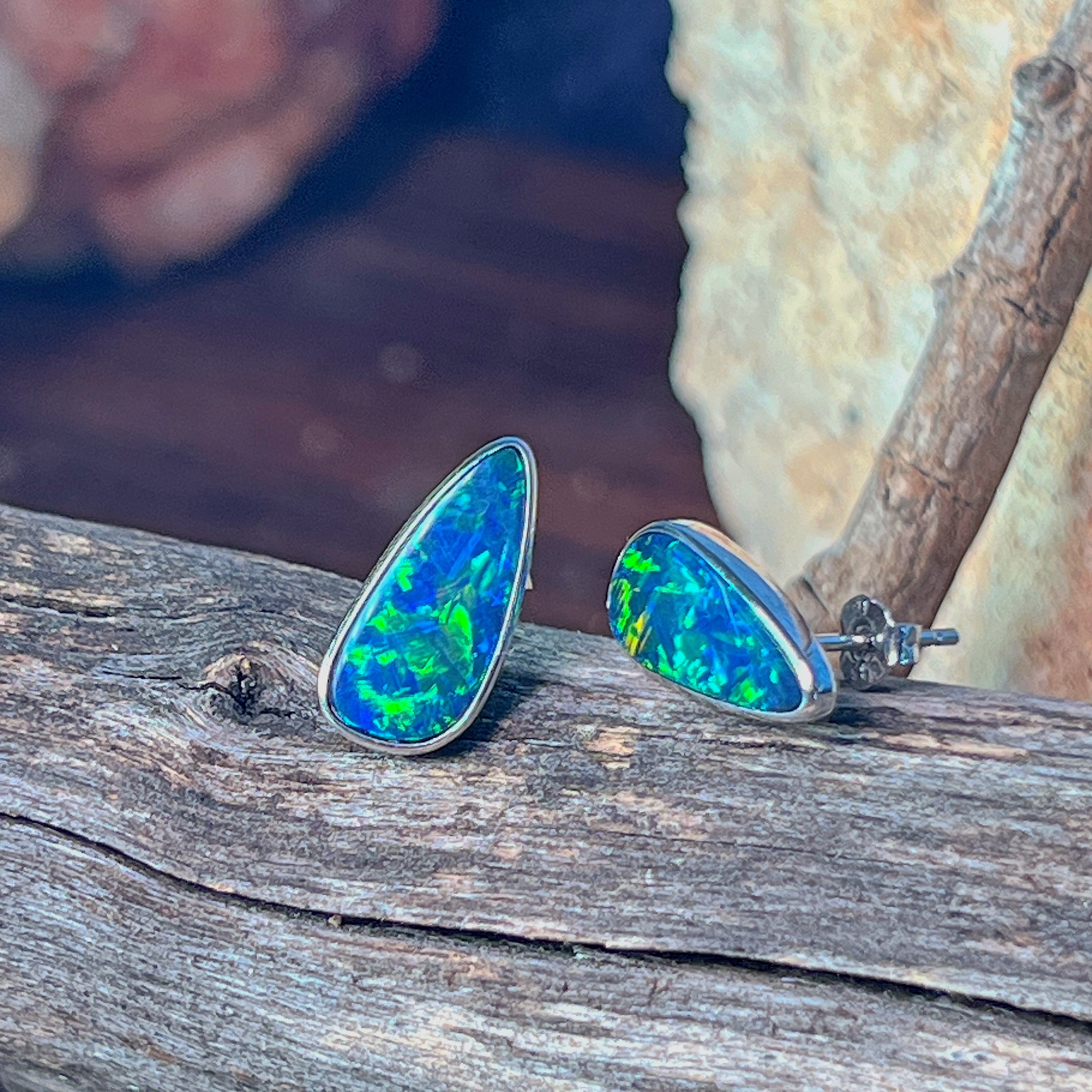 Teardrop opal doublet stud earrings in silver against a dark background, showing green flash