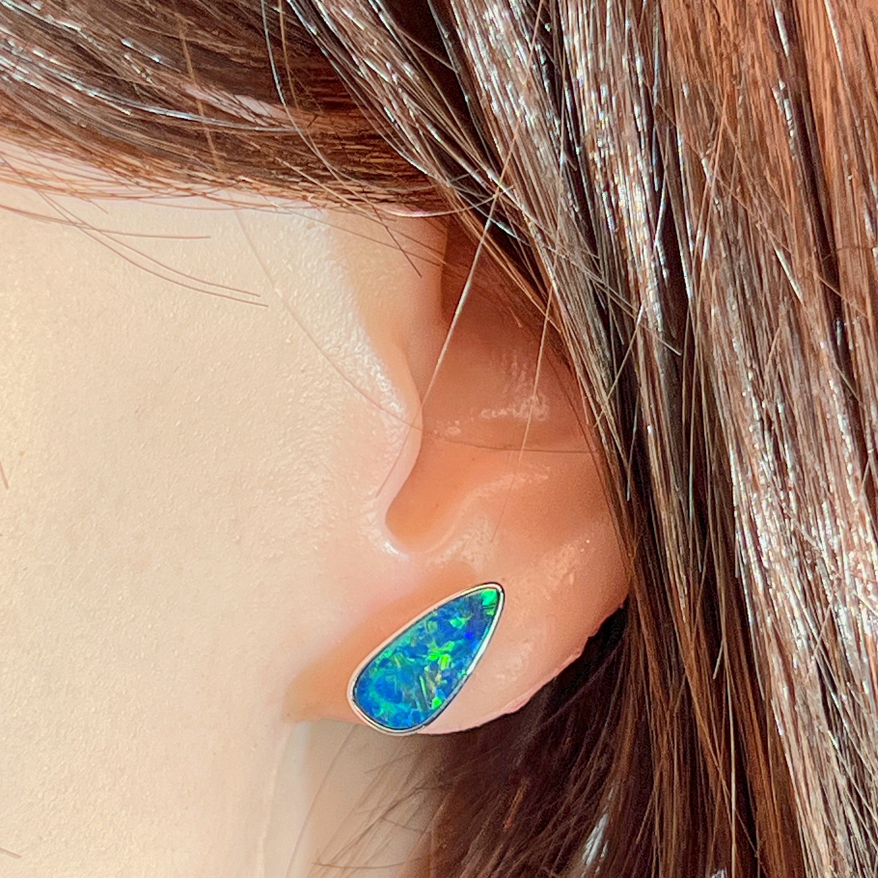Pear-shaped opal doublet stud earring worn on the ear, showing its scale on the earlobe