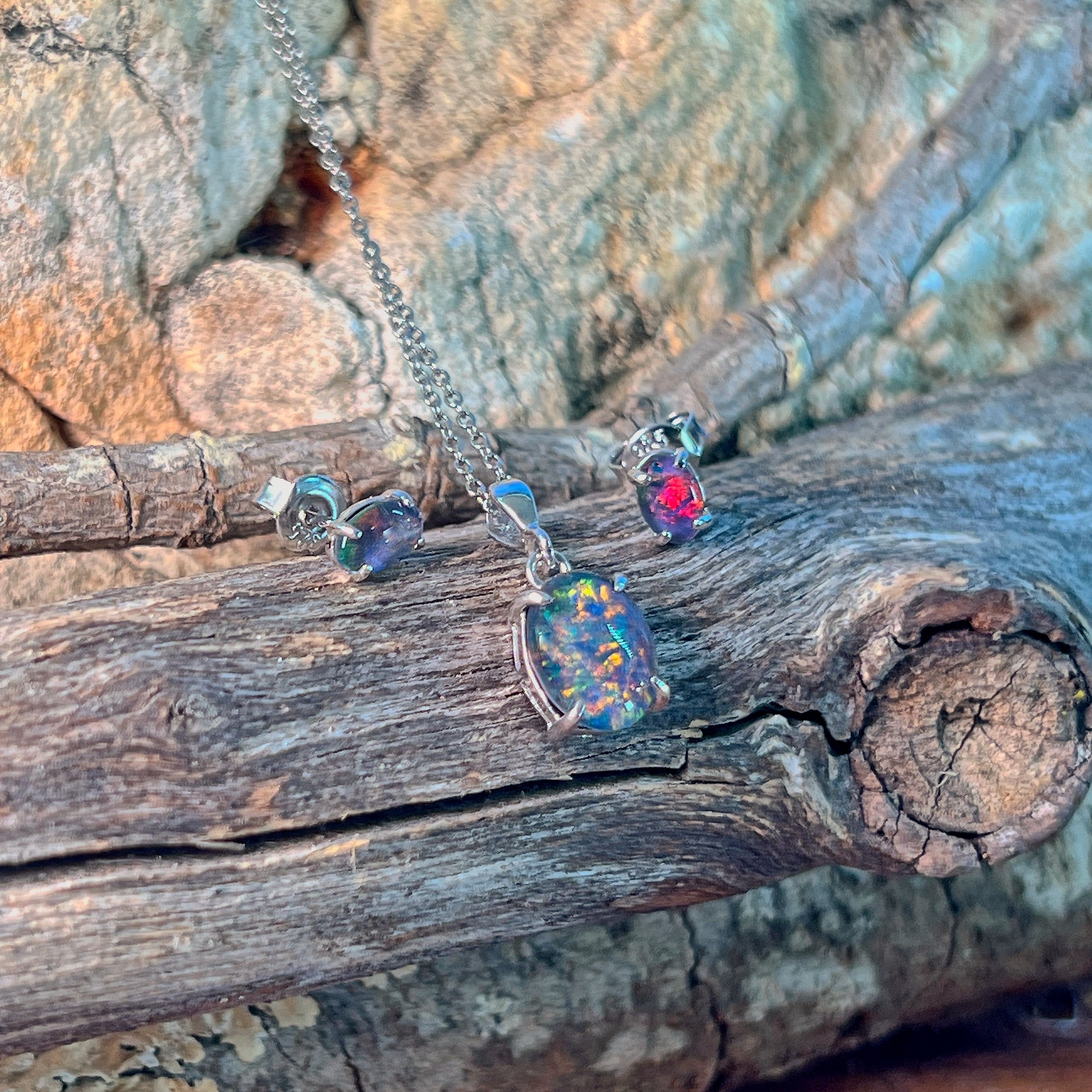 Opal triplet pendant and claw-set studs in silver against driftwood and sandstone