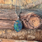 Sterling silver claw-set opal triplet pendant hanging against weathered driftwood