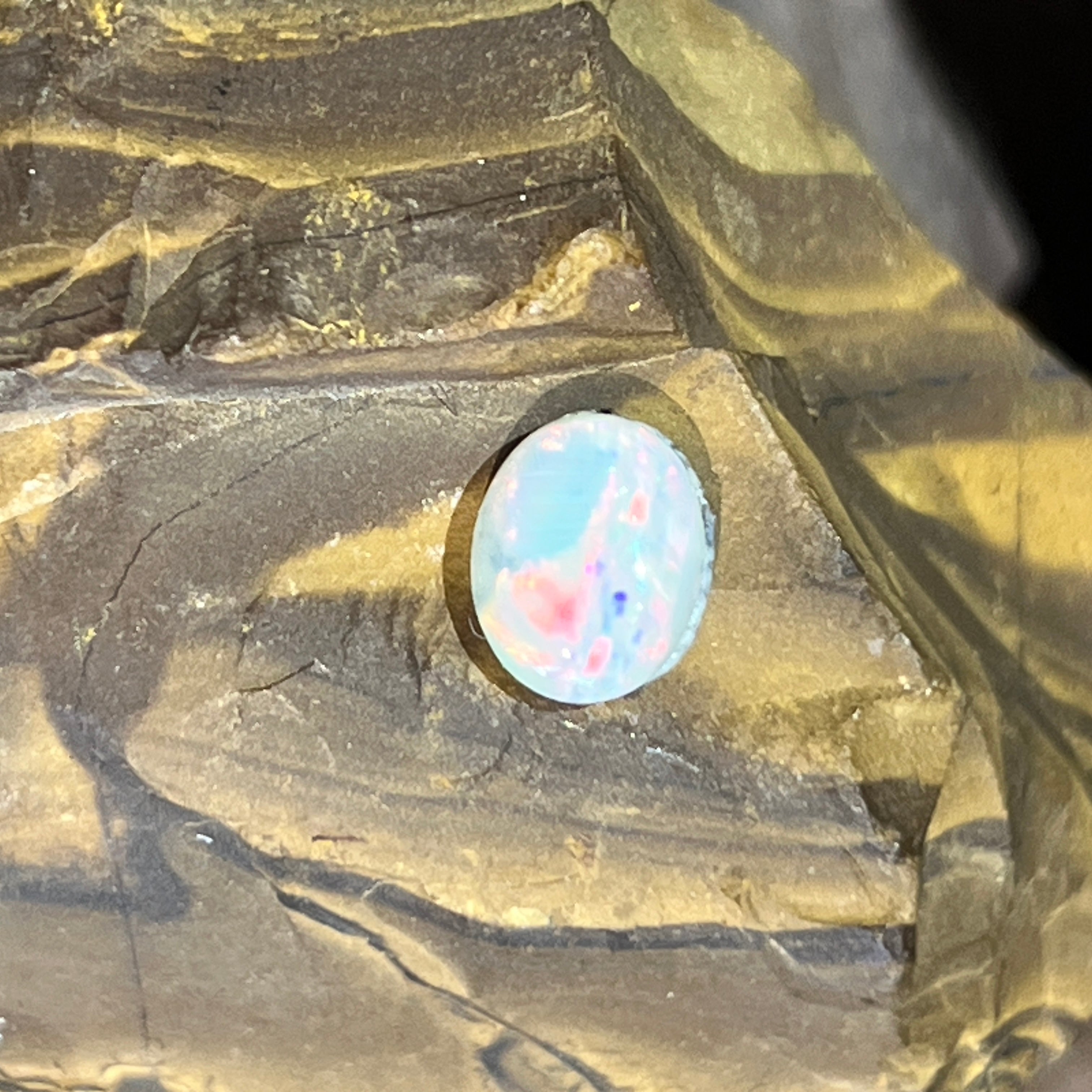 Australian white opal, 1.3ct oval cabochon, on a sunlit ironstone ledge